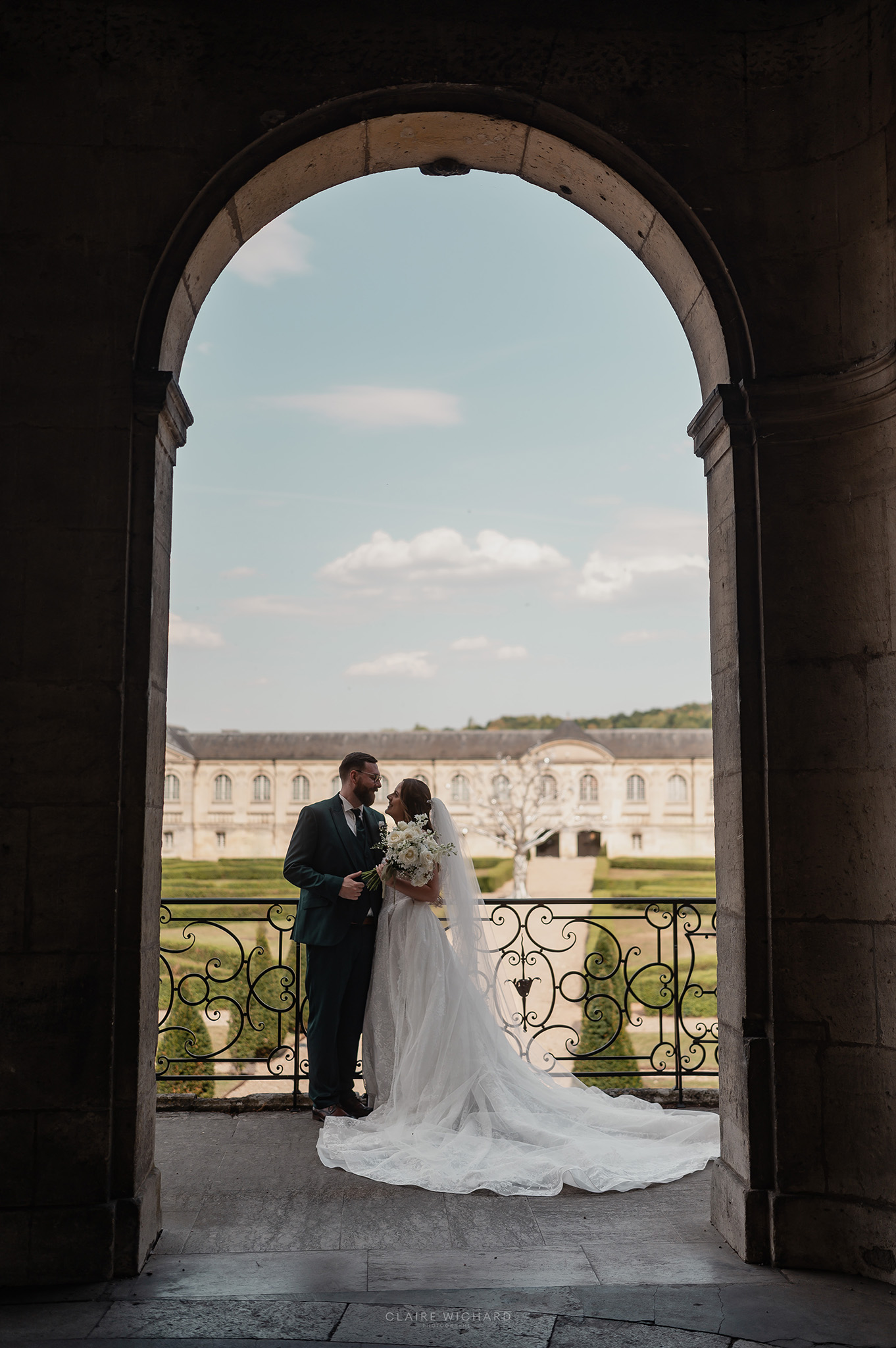 Couple de mariés posant sous les arcades de l'Abbaye des Prémontrés avec vue sur le jardin bordé par la Moselle, photographe de mariage Nancy Claire Wichard