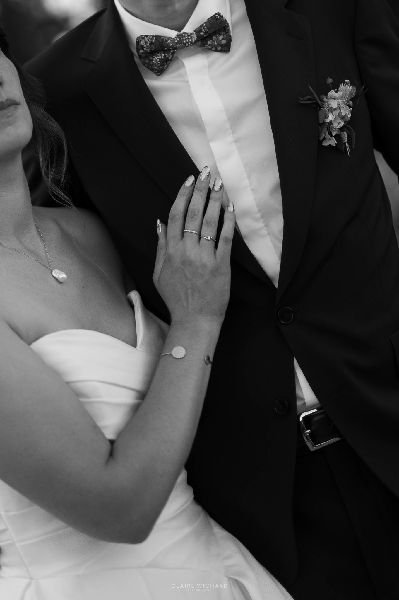Gros plan en noir et blanc sur la main de la mariée et ses alliances posées sur le costume du marié. Photo de mariage près de Nancy par Claire Wichard Photographe.