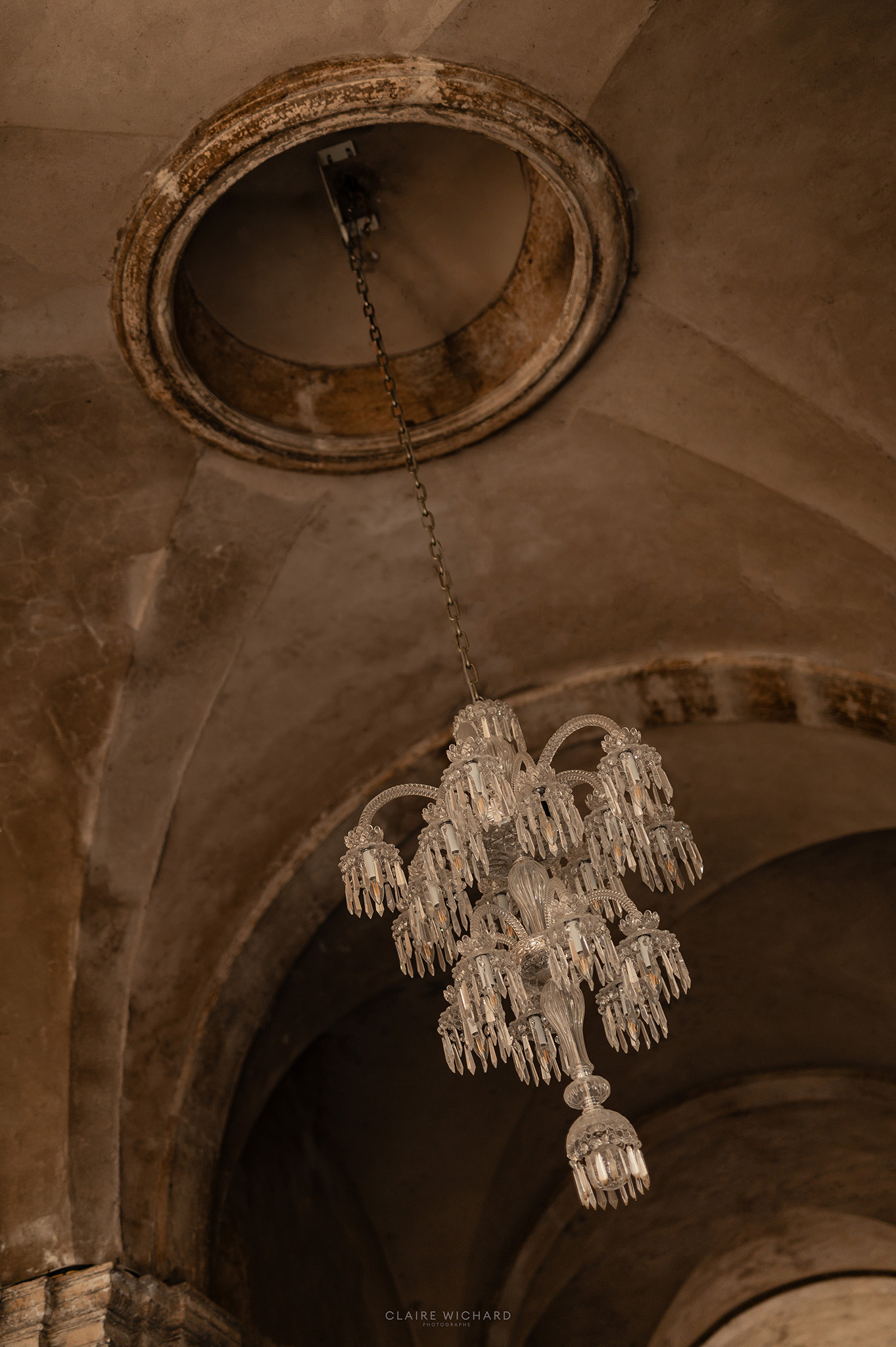 Gros plan sur un lustre en cristal ancien suspendu à une voûte en pierre de l'Abbaye des Prémontrés, reportage de mariage par Claire Wichard à Nancy