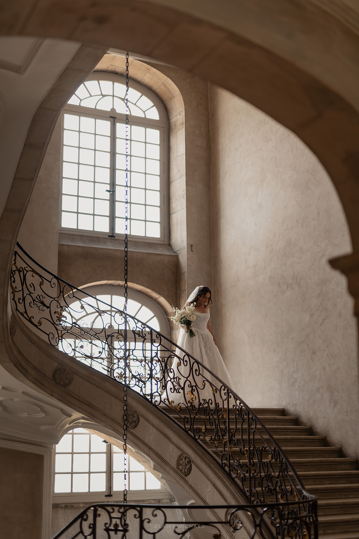 La mariée descend l'escalier monumental en pierre de l'Abbaye des Prémontrés, cadrage sous arche par la photographe de mariage Nancy Claire Wichard