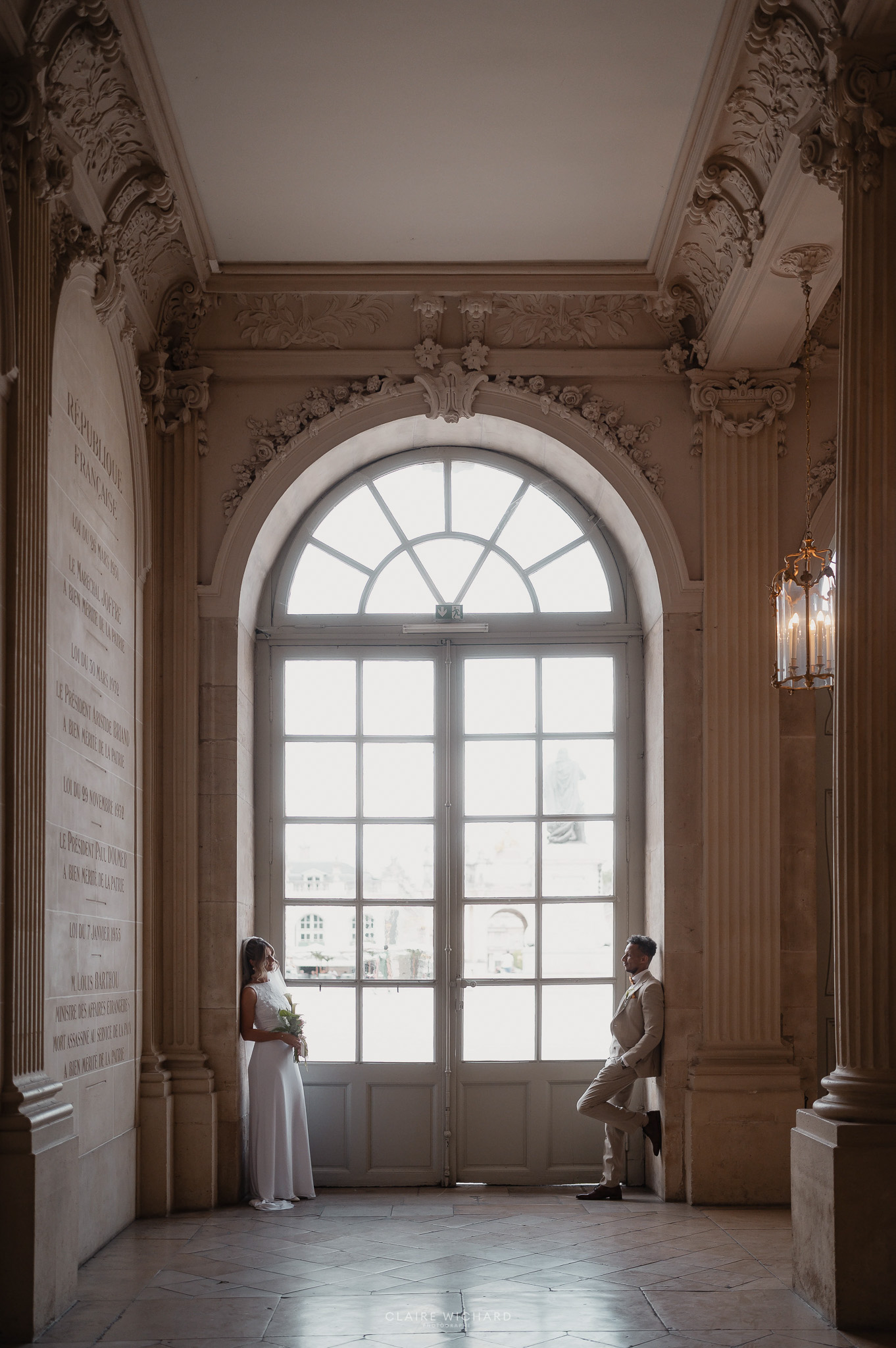Couple de mariés posant devant la grande verrière de la Mairie de Nancy.