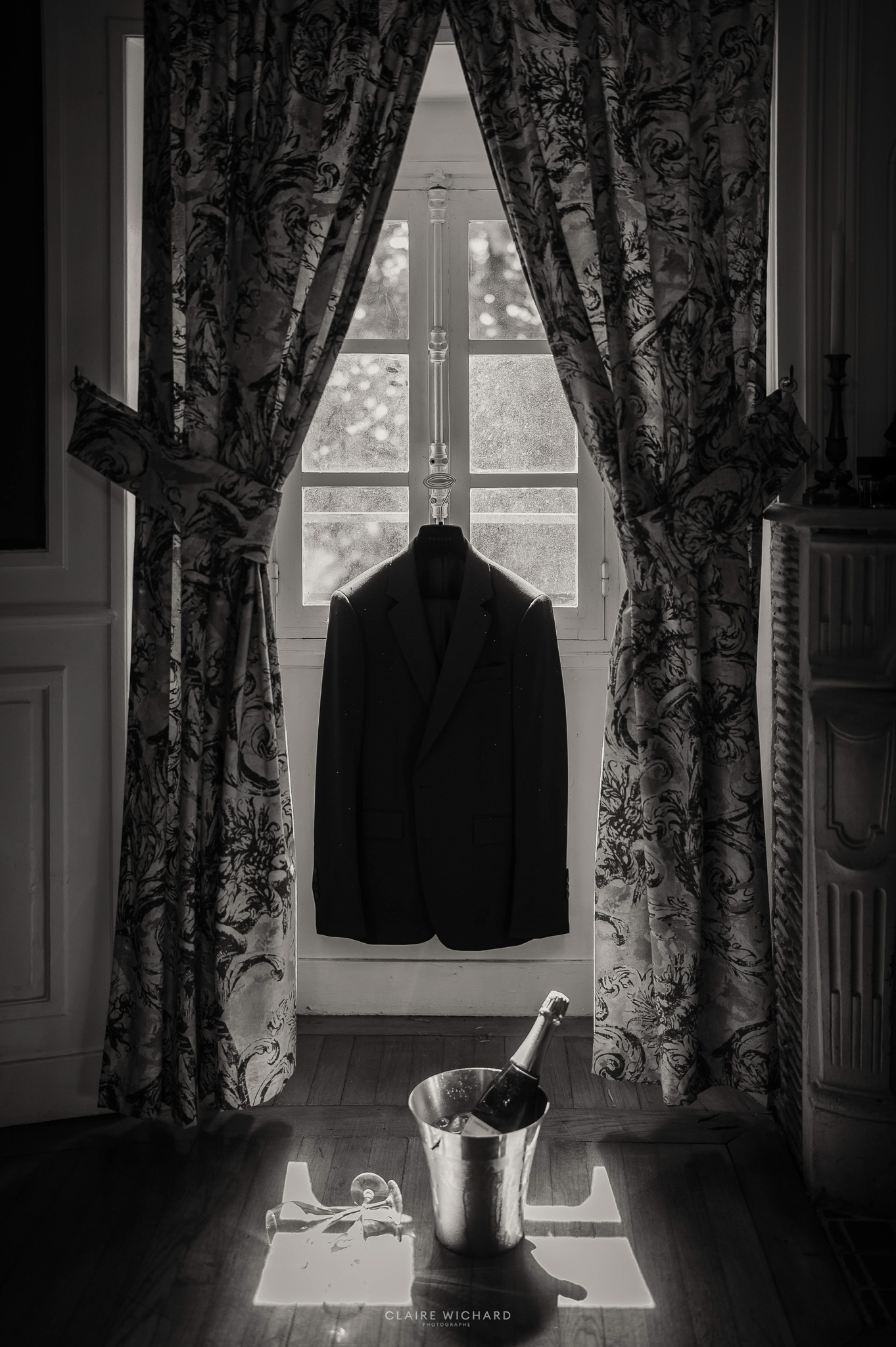 Préparatifs du marié au Château de Hattonchâtel en noir et blanc avec costume suspendu face à la fenêtre, photo Claire Wichard Photographe.