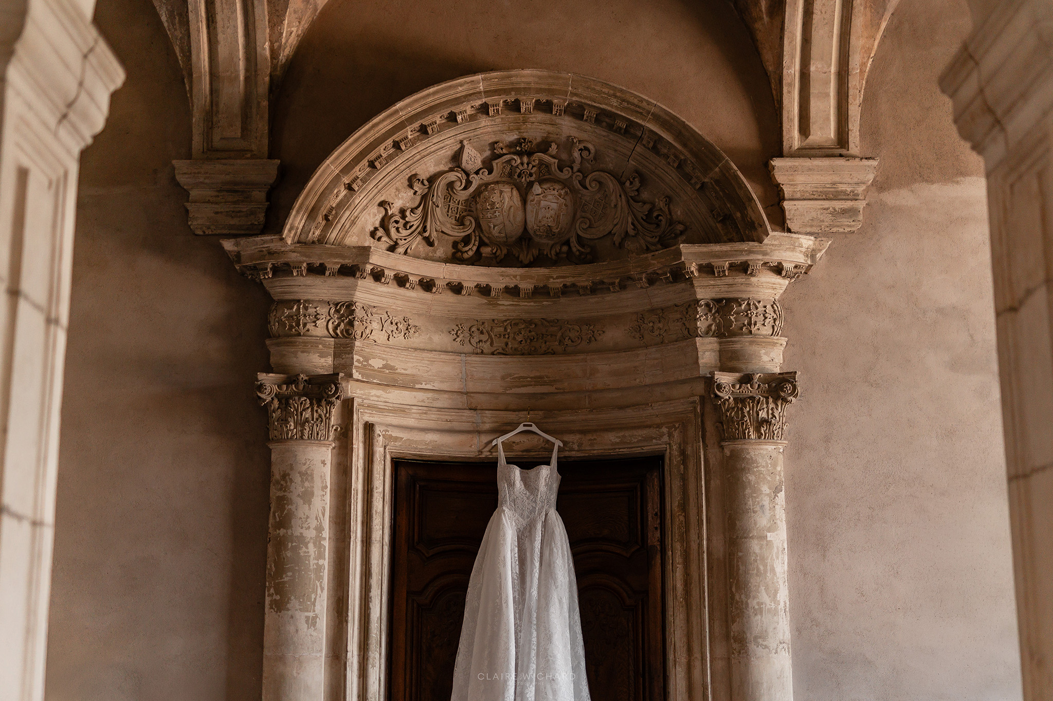 Robe de mariée suspendue élégamment sous un fronton sculpté en pierre de taille à l'Abbaye des Prémontrés, préparatifs de mariage par Claire Wichard à Nancy
